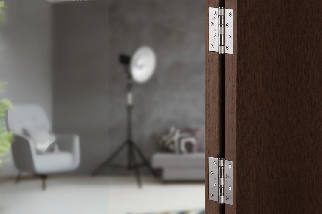The JNF Satin Stainless Steel Ball Bearing Hinge 100x75mm installed on a brown wooden door with a blurred background.