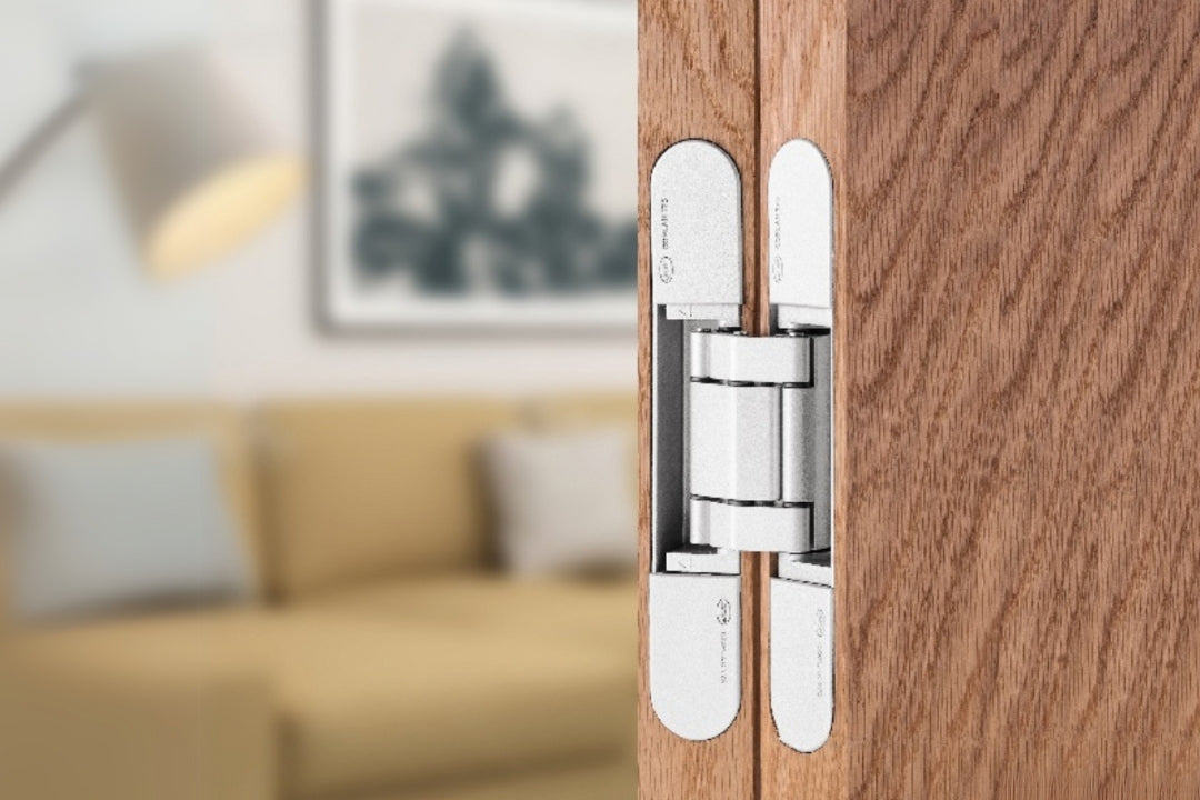 Insitu image of the IN.05.061.W Coplan Hinge installed on a wood grain door with a blurred out lounge room in the background.