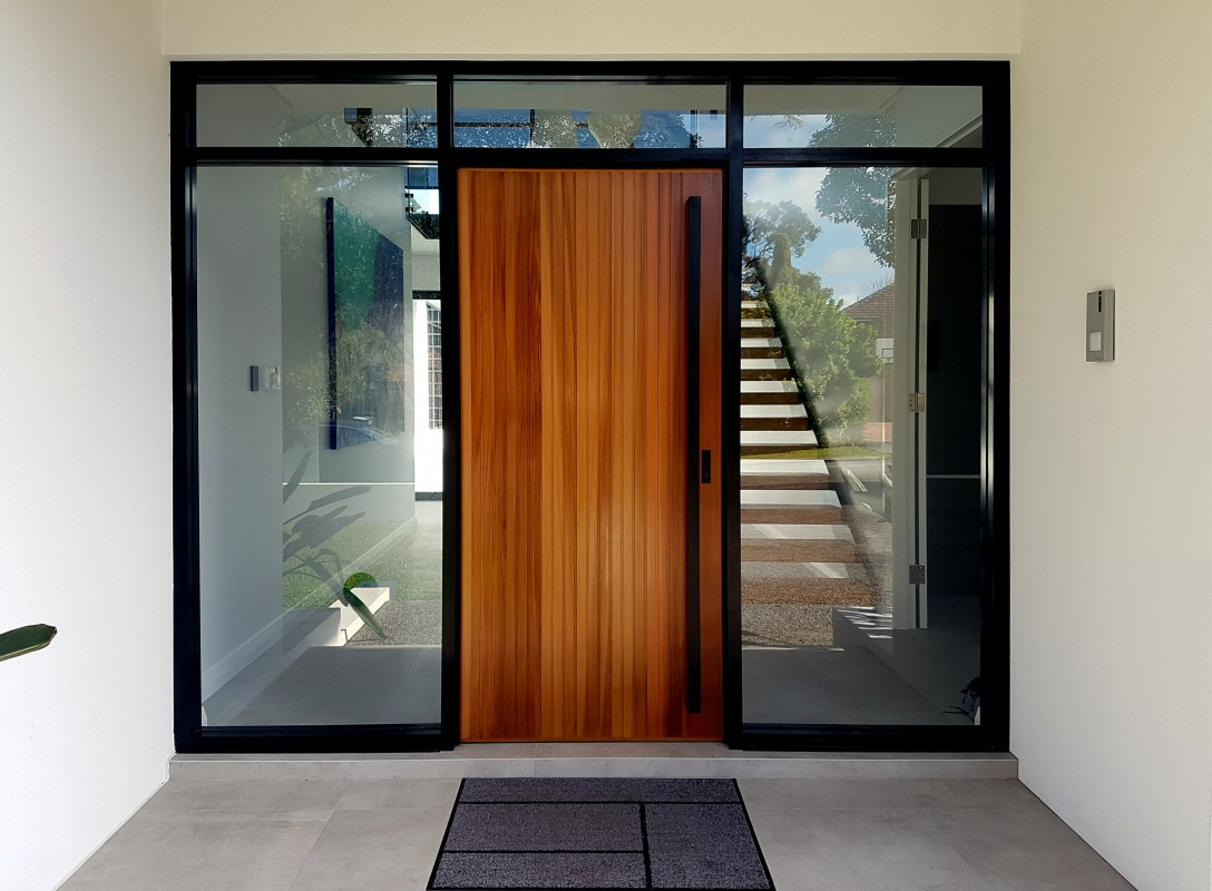 An 1800mm Polo Matt Black pull handle installed on a vanished wooden door with glass on either side of the door.
