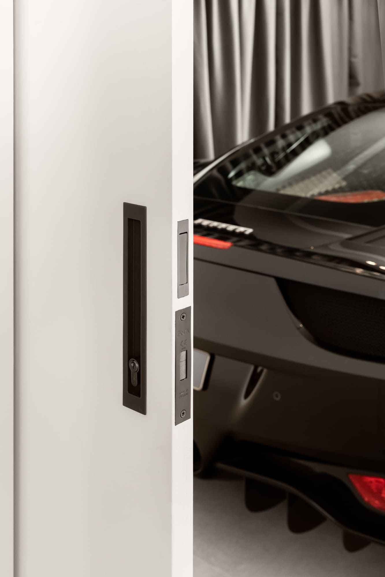Insitu image of the Verve sliding door lock kit in gun metal grey with a garage in the background that has a black sports car in it.