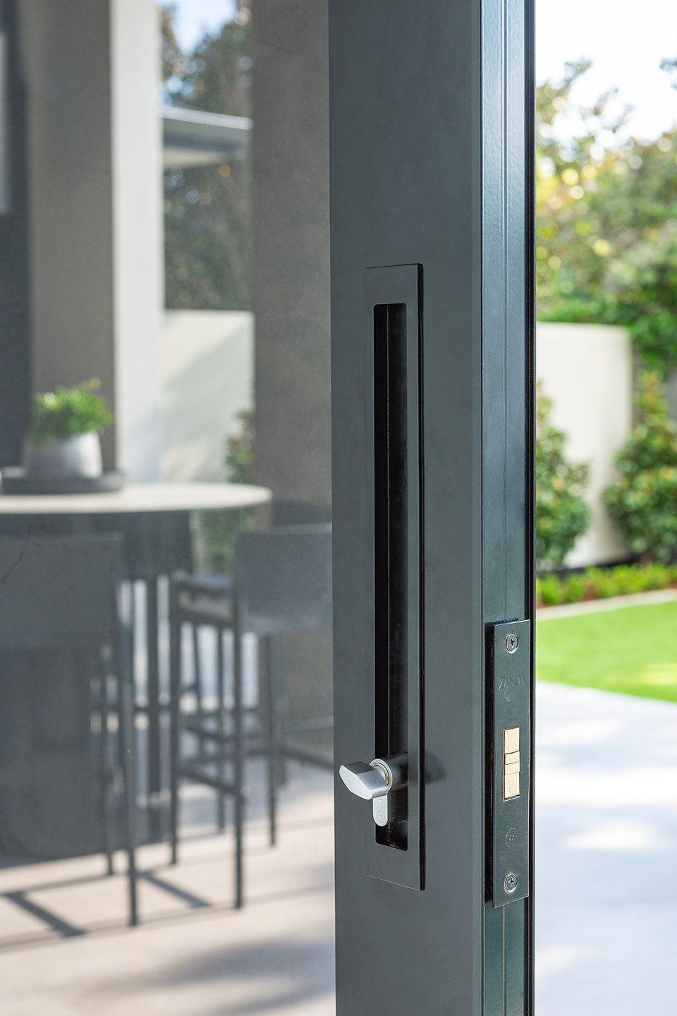 Interior look at the Matt Black sliding door kit installed on a dark grey door with a view to the backyard.