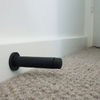 The Matt Black Wall Mount Door Stop on a white skirting and carpet for flooring.