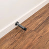 The Zanda Graphite Nickel Round Wall Door Stop 85mm installed onto the skirting board with a wooden floor in the picture as well.