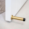 The Satin Brass Wall Mount Door Stop installed on a white door that is slightly open.