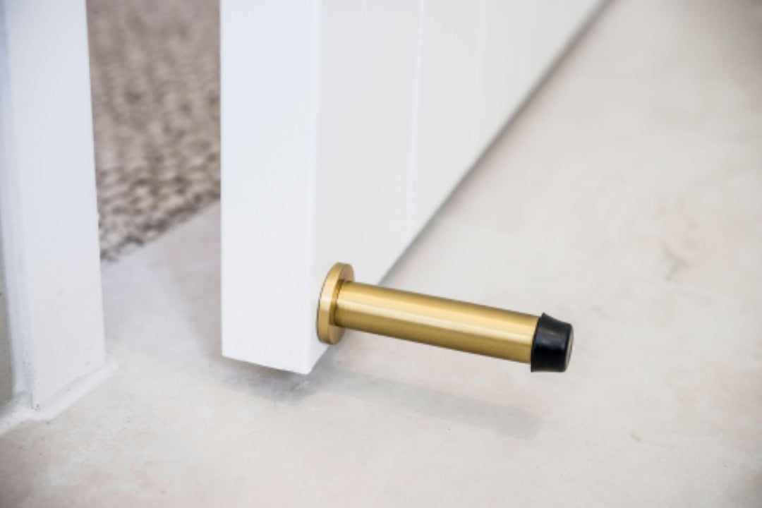 The Satin Brass Wall Mount Door Stop installed on a white door that is slightly open.