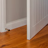 The Zanda Square Skirting Mount Door Stop 80mm Brushed Nickel 5262.BN installed on white skirting with a white door and polished wooden floors.