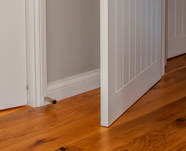 The Brushed Nickel Square Wall Mount Door Stop installed on white skirting and on wooden floors.