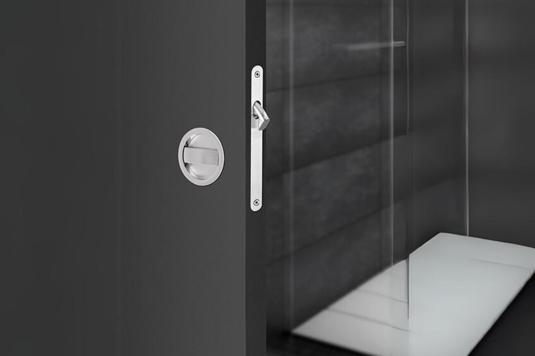 Insitu image of the Visca Satin Chrome Sliding Door Privacy Kit installed on a black door with a bathroom in the background.