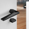 Archi Sketch Titanium Black PVD lever handle on a white door with a blurred background.