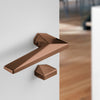Archi Sketch Titanium Copper lever handle on a white door with a blurred wooden floor background