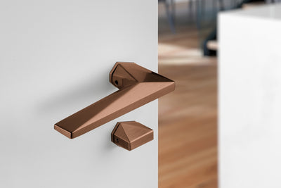 Archi Sketch Titanium Copper lever handle on a white door with a blurred wooden floor background