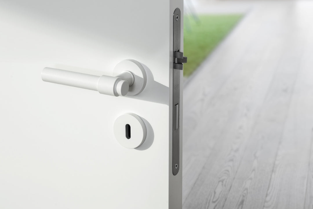 Insitu image of the IN.00.145.W Brooklyn White Door Handle set installed on a white door with an outdoor footpath in the background.