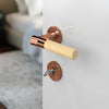 JNF Wood Nature IN.00.381.BB.TCO Bamboo Titanium Copper lever handle on a white door with a blurred background.