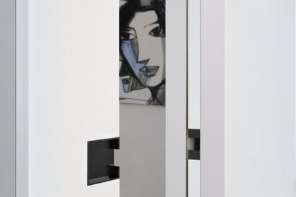 Insitu photo of the Matt Black Pocket Door Flush Pull 100mm on off white doors with a painting of a face in the background.