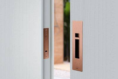 Image of the IN.20.925.TCO Copper Sliding Door Privacy Kit installed on an off white door.