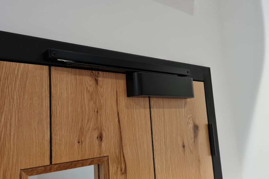 Insitu image of the Matt Black Door Closer with Slide Arm installed on a wooden door.