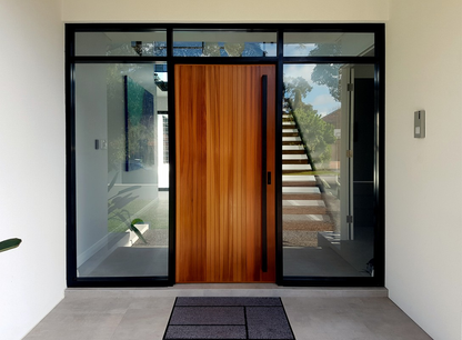 An 1800mm Ultra Matt Black pull handle installed on a vanished wooden door with glass on either side of the door.