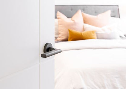 The Urban Gun Metal Grey Door Handle on a white door looking into a bedroom.