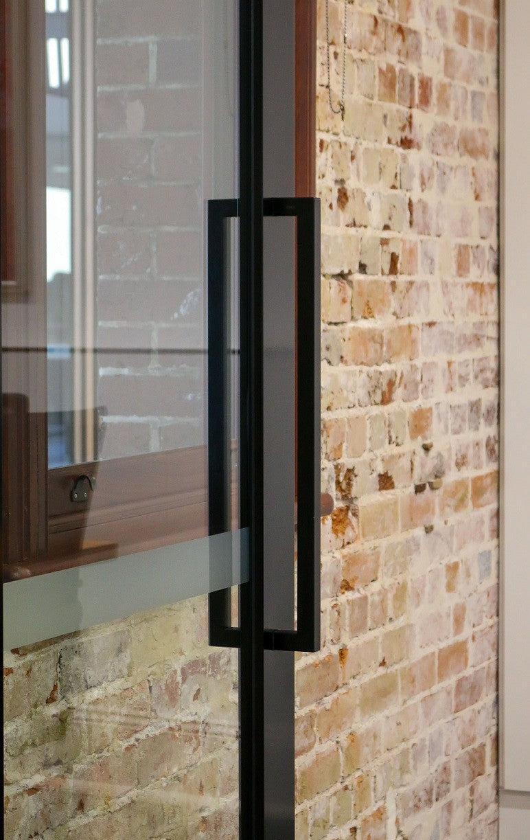 The Toorak Matt Black pull handle installed on a glass door.