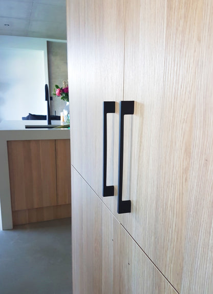 Insitu image of the Urban Matt Black Cabinet Handle installed on wooden cabinetry.