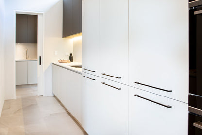 Insitu image of the Urban Matt Black Cabinet Handle installed on white cabinetry in a kitchen.